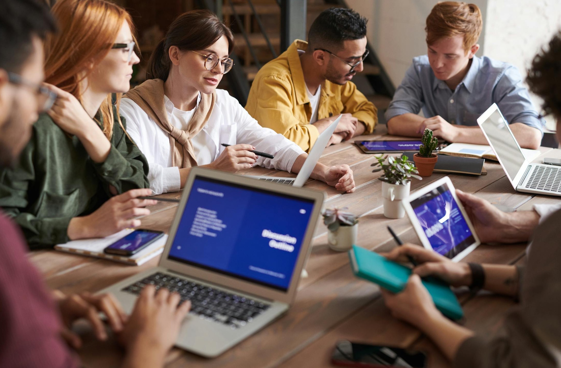 Three professionals engaged in a discussion around a laptop, representing successful collaboration, talent acquisition, and new business opportunities facilitated by strong LinkedIn presence.